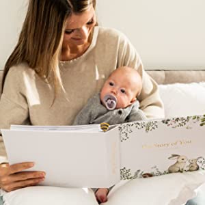 Mom says hello to baby. Baby and mom read the baby memory book the story of you on the bed.